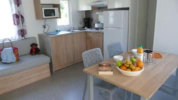 Cozinha compacta com micro-ondas, fogão e geladeira. Há uma mesa de jantar com uma cesta de frutas e um livro.