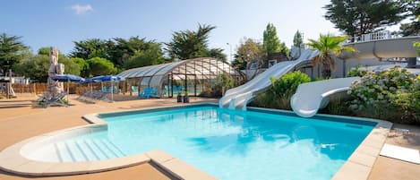 Una piscina con dos toboganes, sillas de descanso y una zona de estar cubierta.