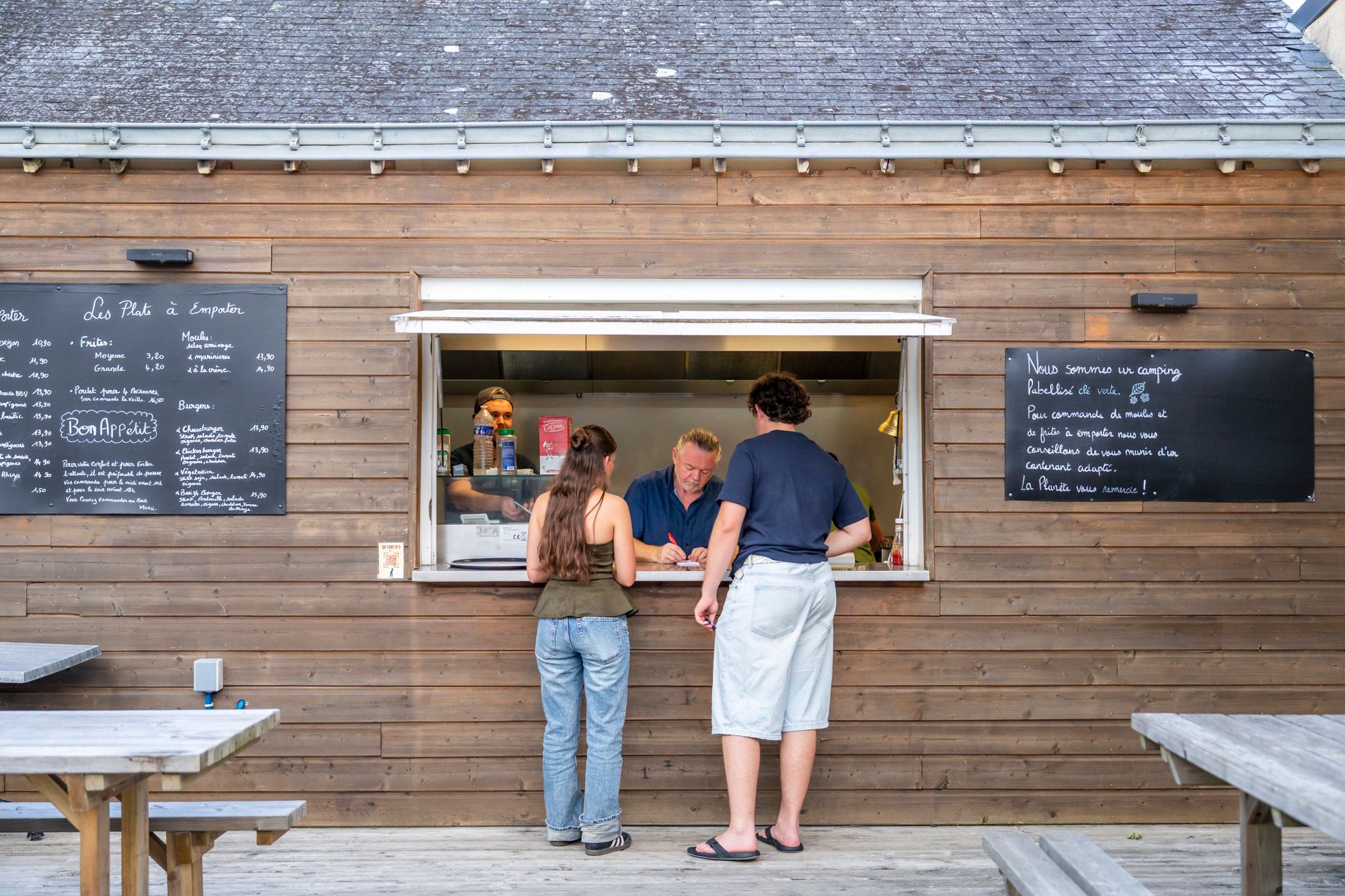 Un bâtiment en bois avec un tableau noir servant de menu, où sont indiqués les plats proposés et leurs prix.