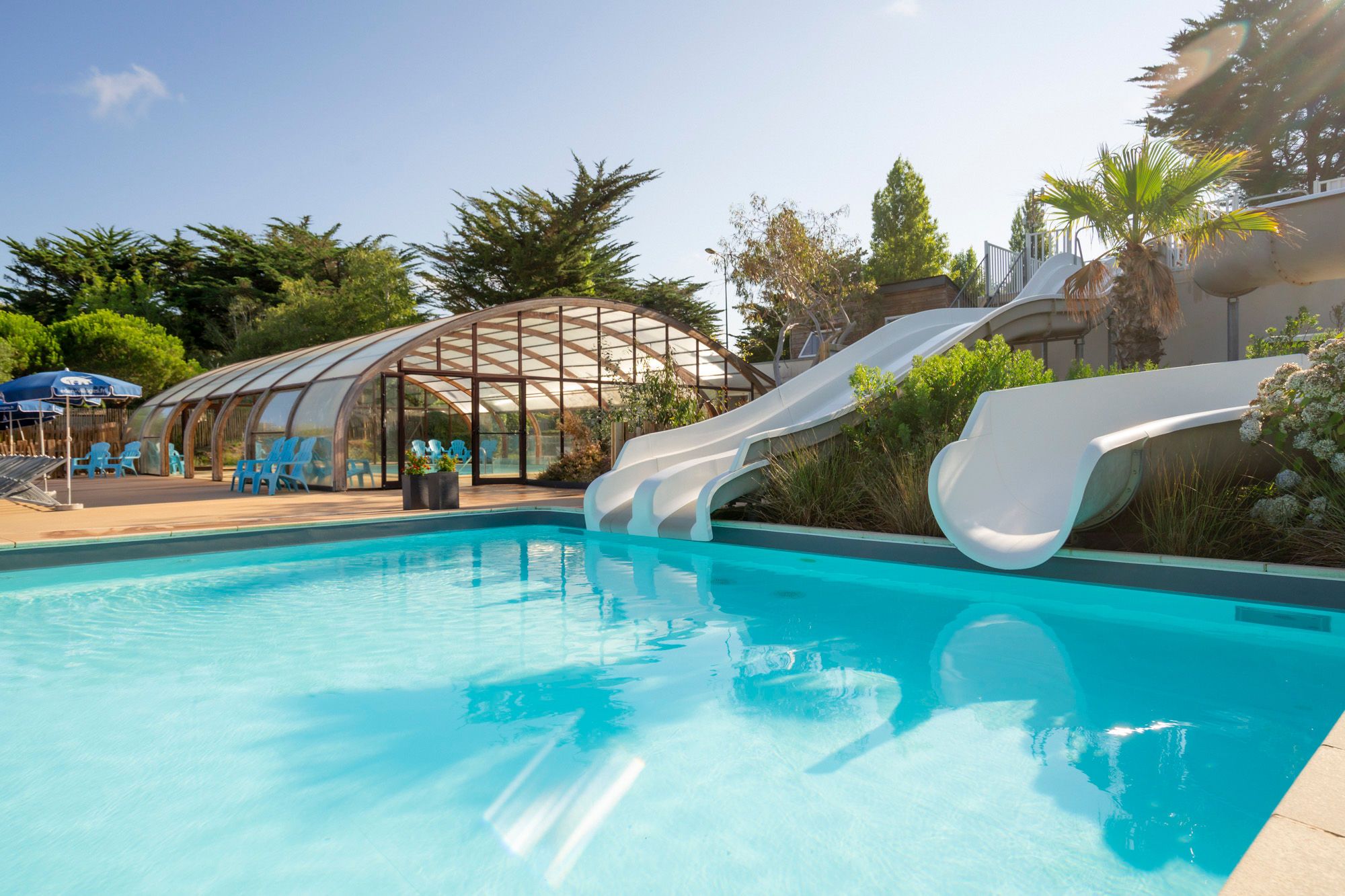 A swimming pool with a slide, surrounded by lounge chairs and a covered seating area.