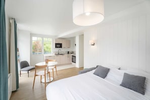 Een moderne slaapkamer met een groot bed, een eethoek met een tafel en stoelen, en een kitchenette.