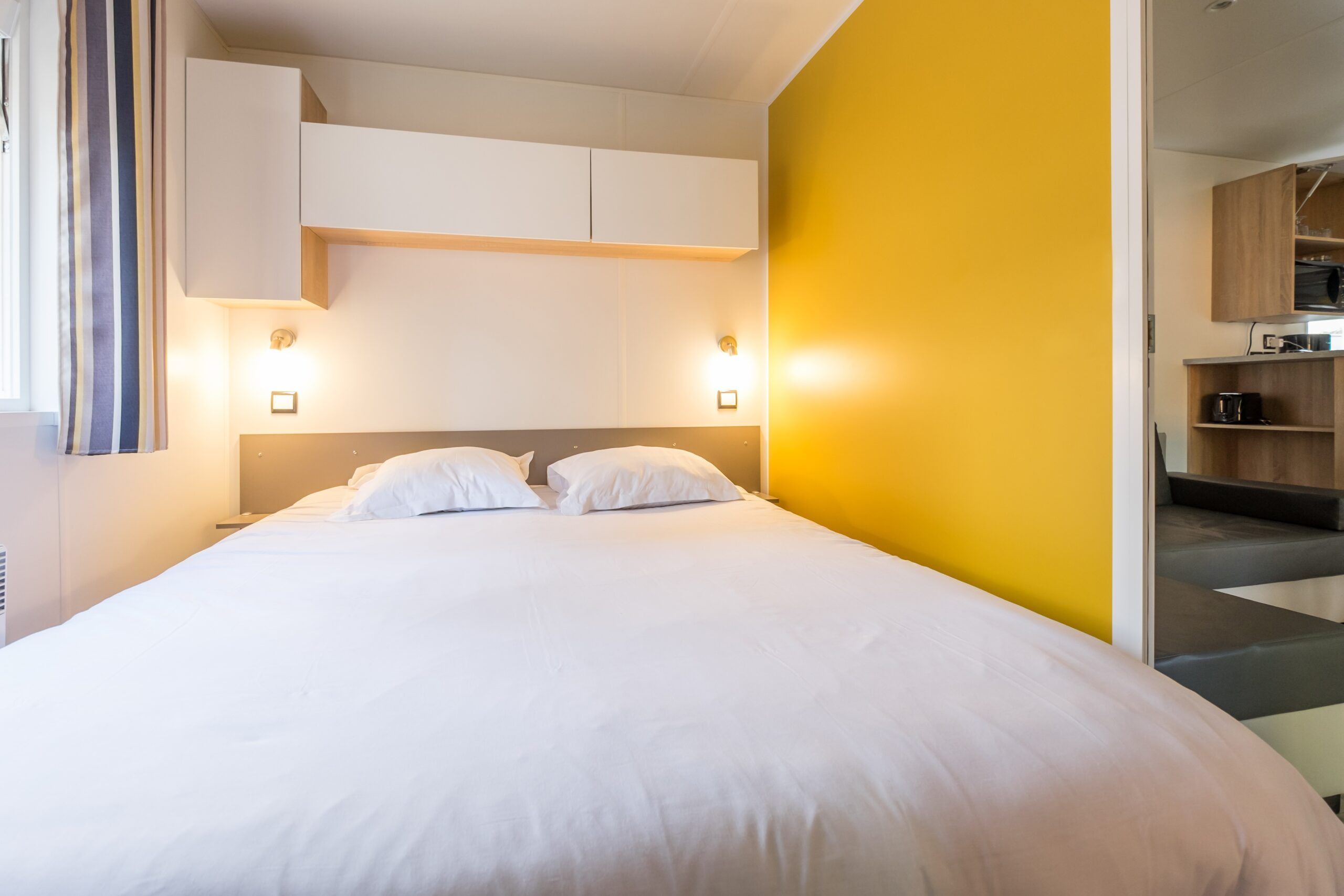 Habitación de hotel con una cama grande, armario empotrado y una pared de acento amarillo brillante.