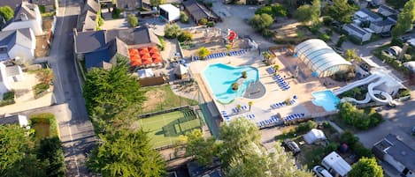 Vista aérea de una zona residencial con piscina, cancha de tenis y tobogán de agua.