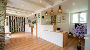 Un espace d’accueil comprenant un comptoir de réception en bois, un pilier en pierre et une plante en pot.