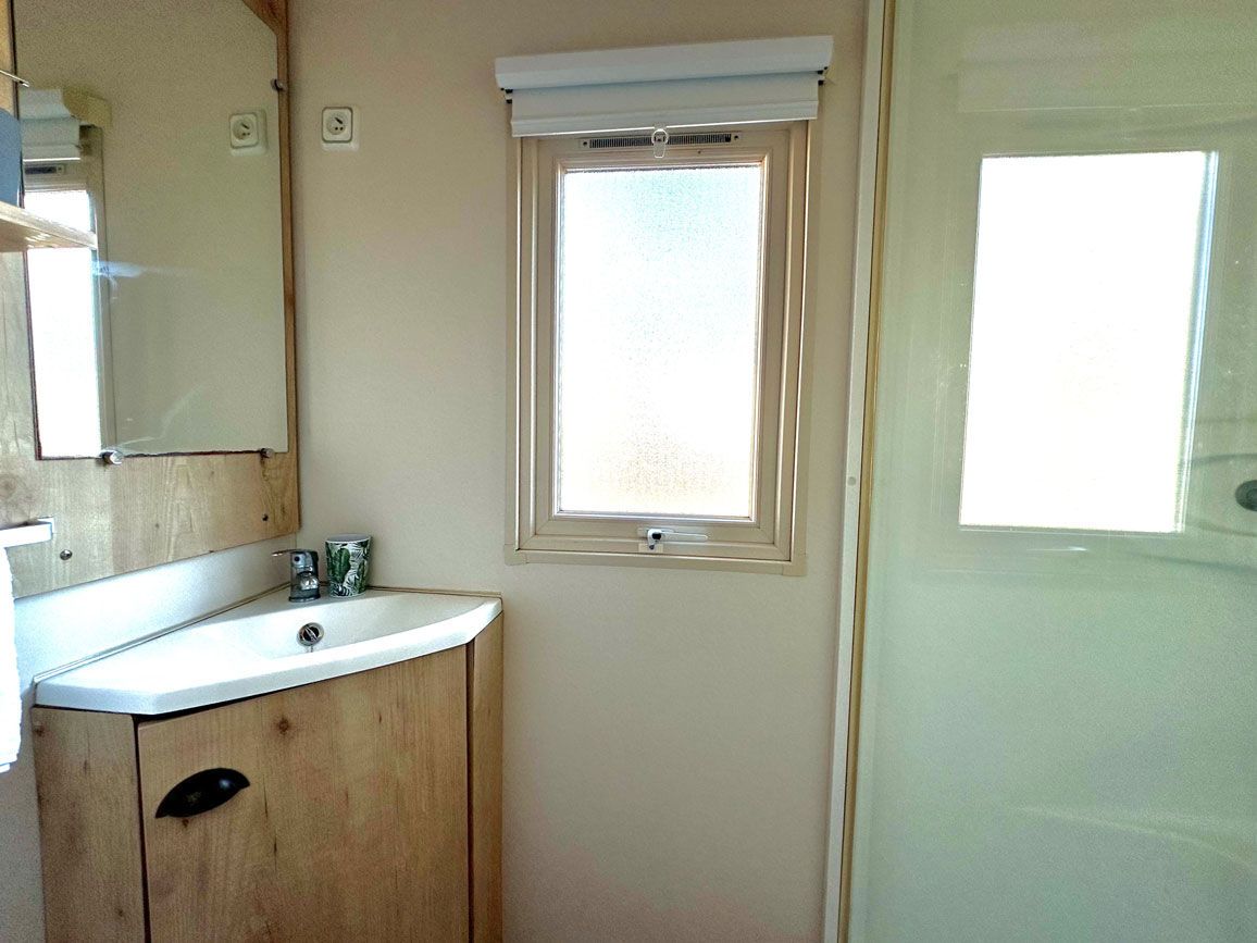 Een badkamer met een houten kastje, een witte wastafel, een spiegel en een raam.
