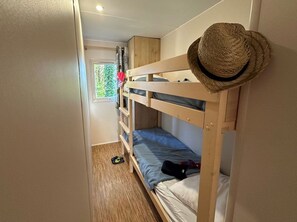 Une chambre avec un lit superposé, un chapeau posé sur la tête de lit, une fenêtre avec des rideaux et une porte.