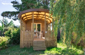 Un belvédère en bois, agrémenté d’un banc et d’une table, entouré de verdure.