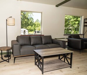 A modern living room with a sofa, coffee table, and a view of a vehicle through large windows. - Beautiful & quiet 3-bedroom house in downtown Talkeetna perfect for any getaway (Talkeetna)