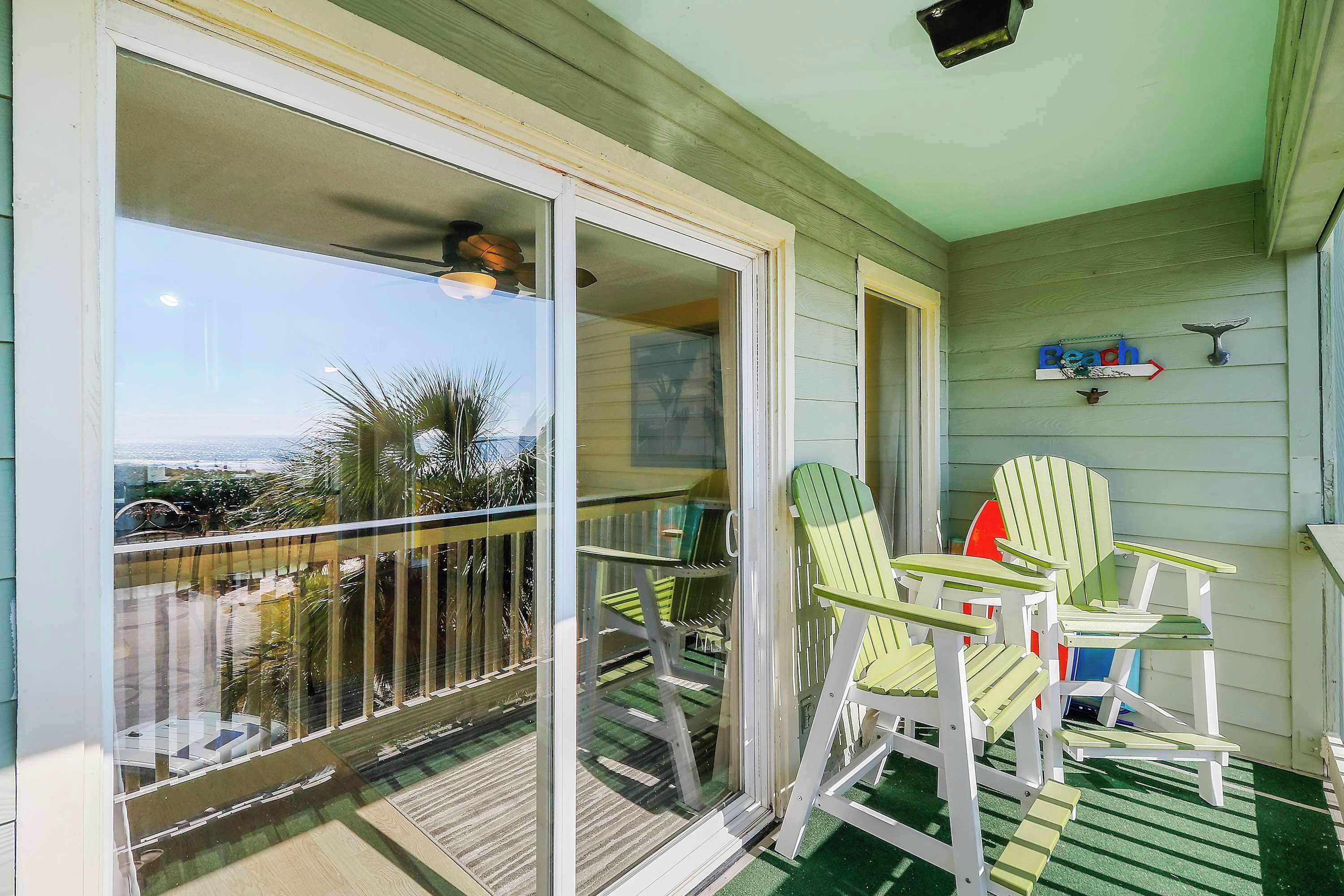 Een balkon met uitzicht op een stadslandschap, twee groene Adirondack-stoelen en een kleine tafel.