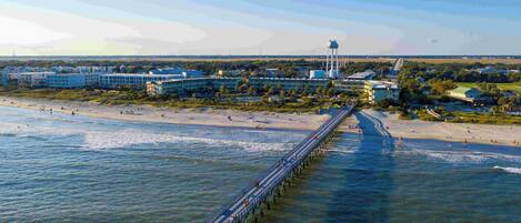 A coastal area with a long pier extending into the water, a beach, and buildings in the background.