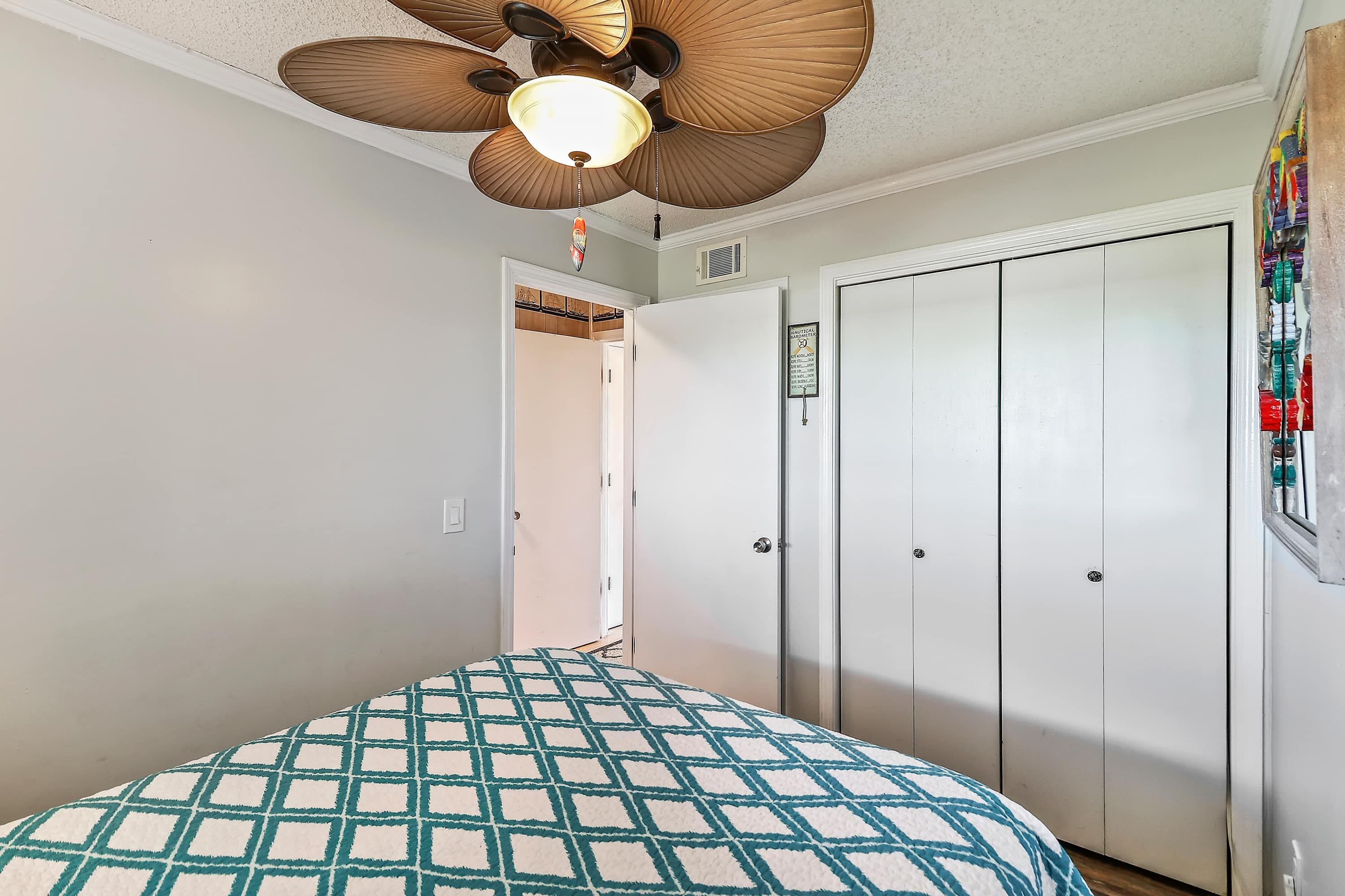 Un dormitorio con una cama, ventilador de techo y armario.