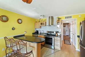 A kitchen with a central island, wooden cabinets, stainless steel appliances, and a yellow wall. - Front Beach Isle of Palms Sea Cabin! (Isle of Palms)