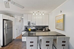 A modern kitchen with white cabinets, a stainless steel refrigerator, a built-in oven, and a coffee maker. - Isle of Palms Sea Cabin with beach view! Pool, fishing pier, and beach access. (Isle of Palms)