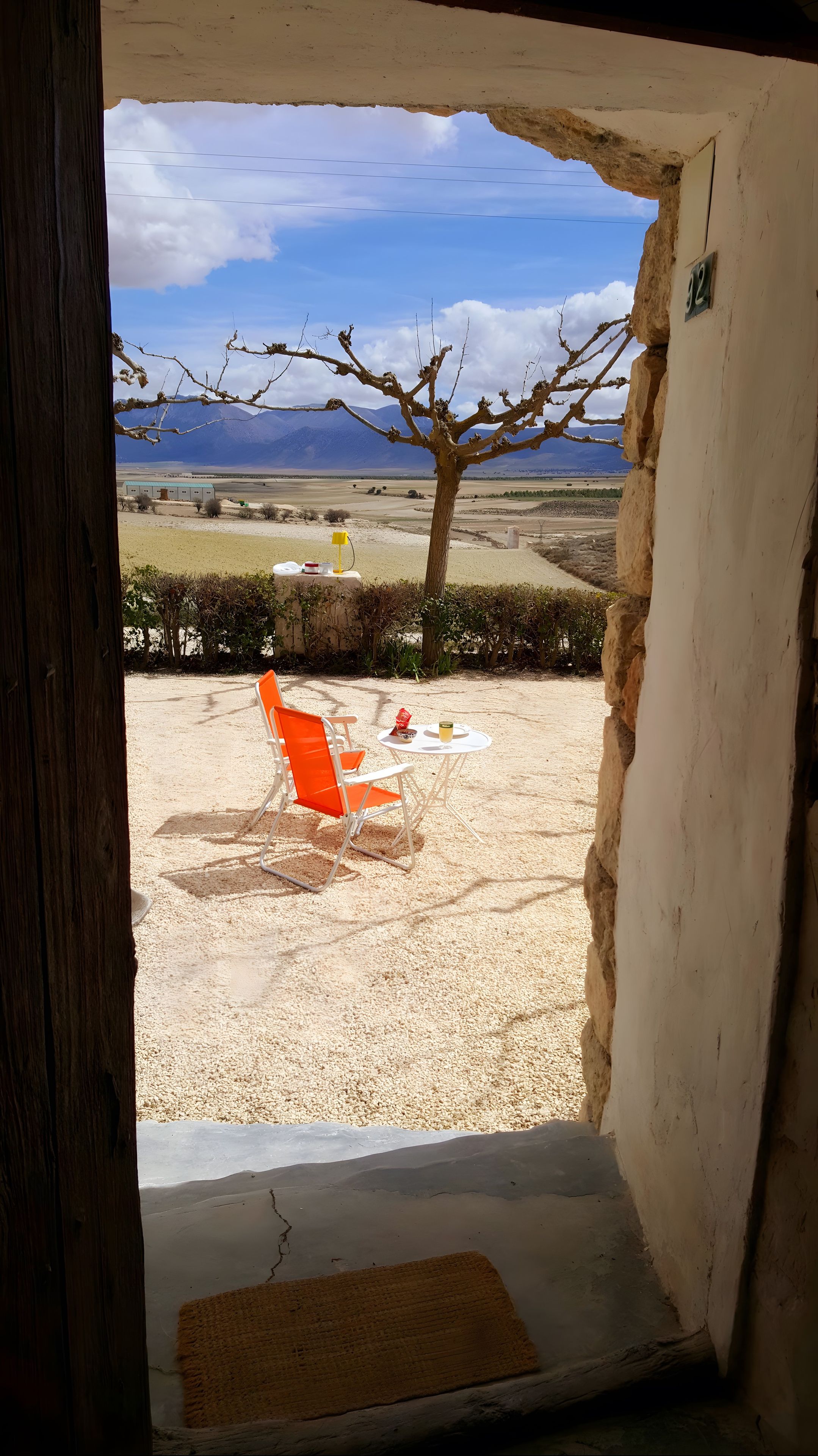 Una puerta que da a un espacio al aire libre con una mesa, sillas y vistas a montañas.