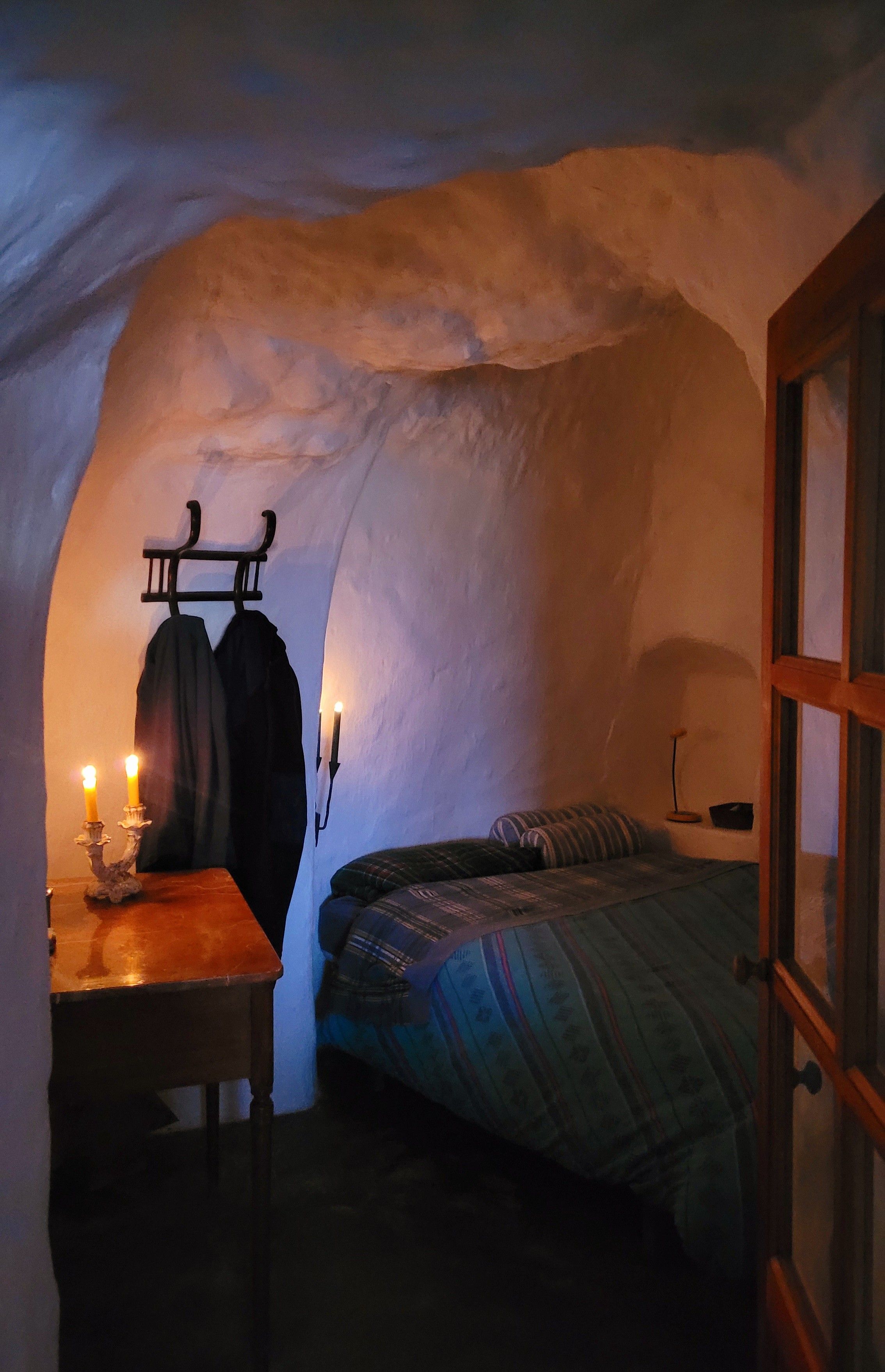Um quarto aconchegante com uma cama, uma mesa com uma vela e um cabideiro.