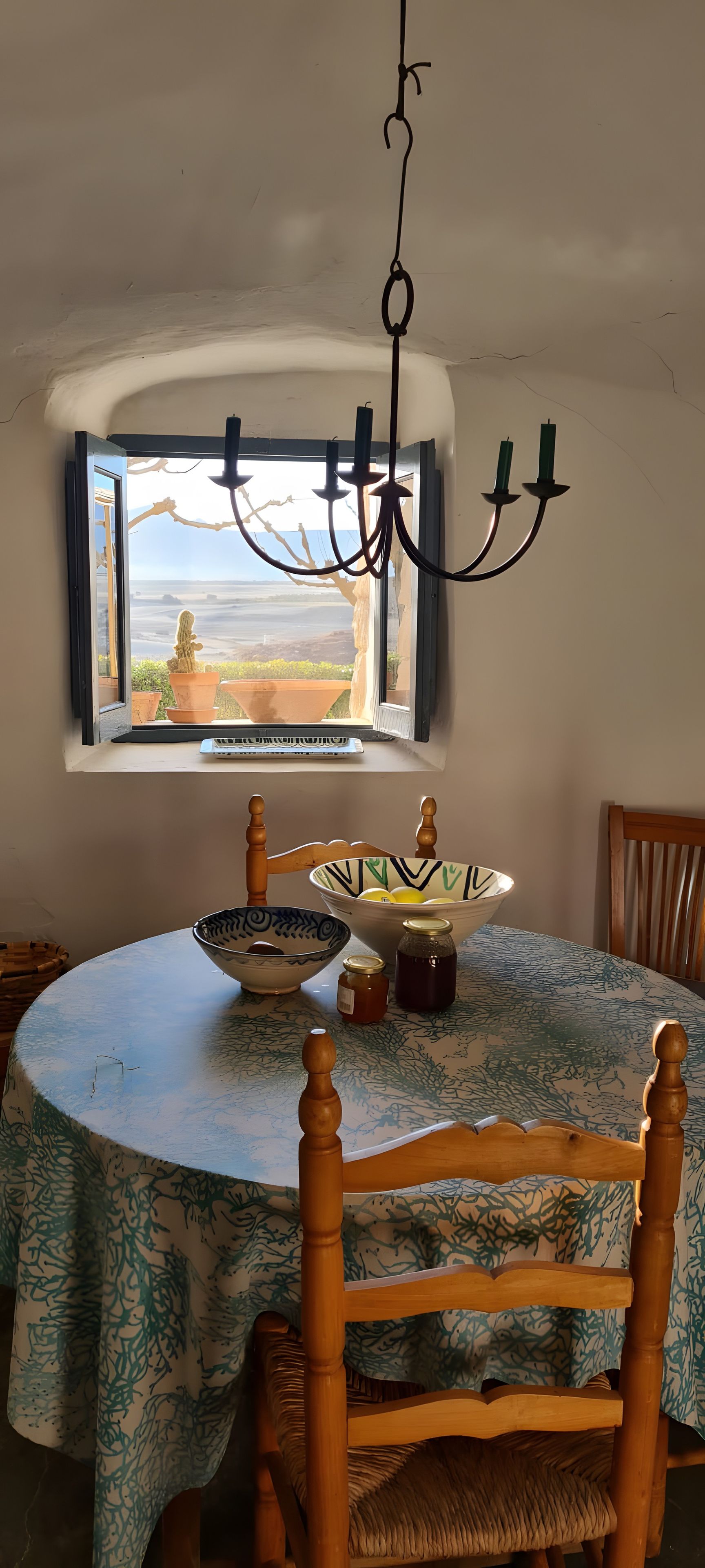 Un comedor con una mesa dispuesta para dos, una araña y un ventanal con vistas al paisaje.