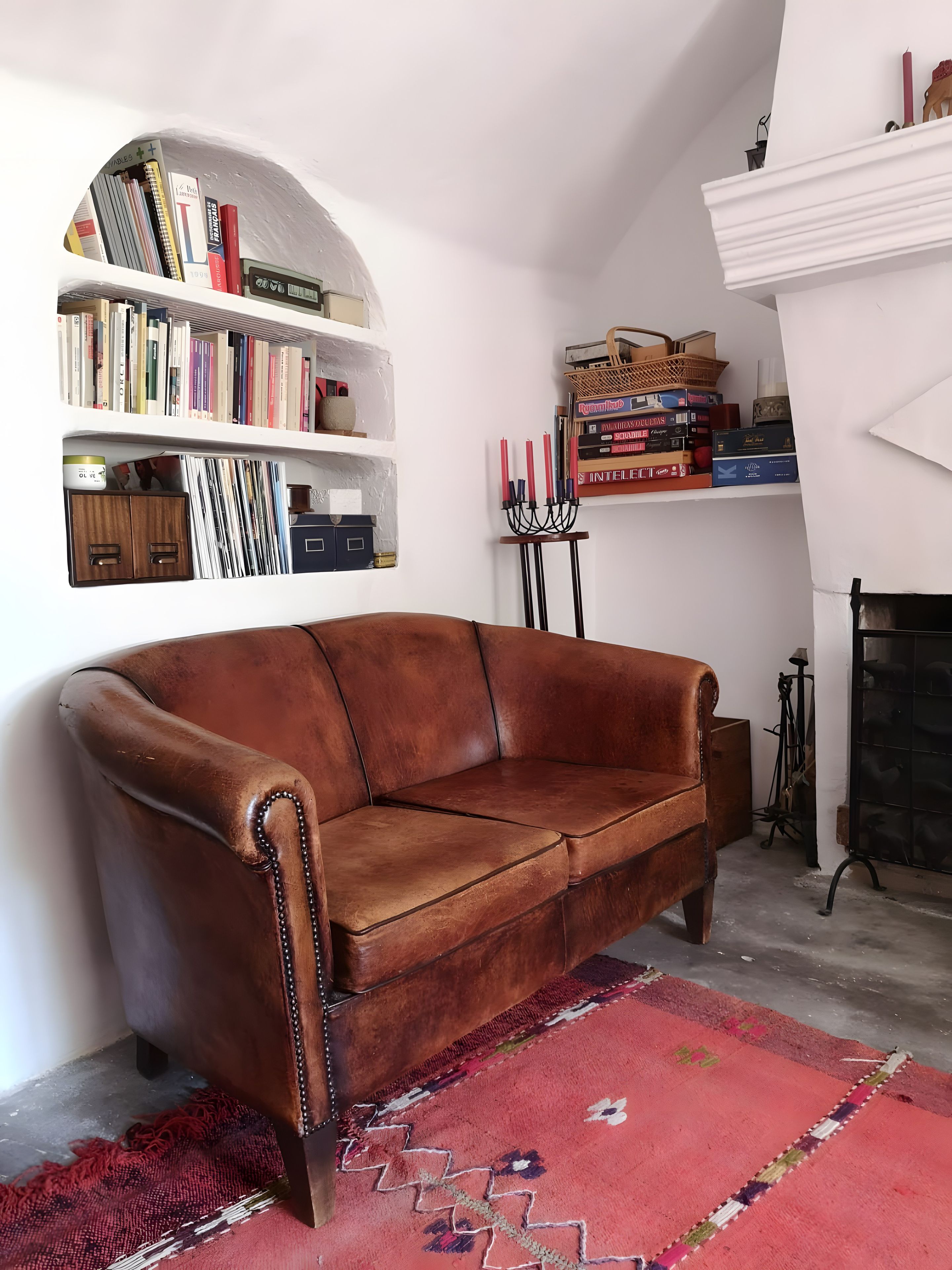 Un sofá de cuero marrón en una habitación con pared blanca, una estantería y una chimenea.