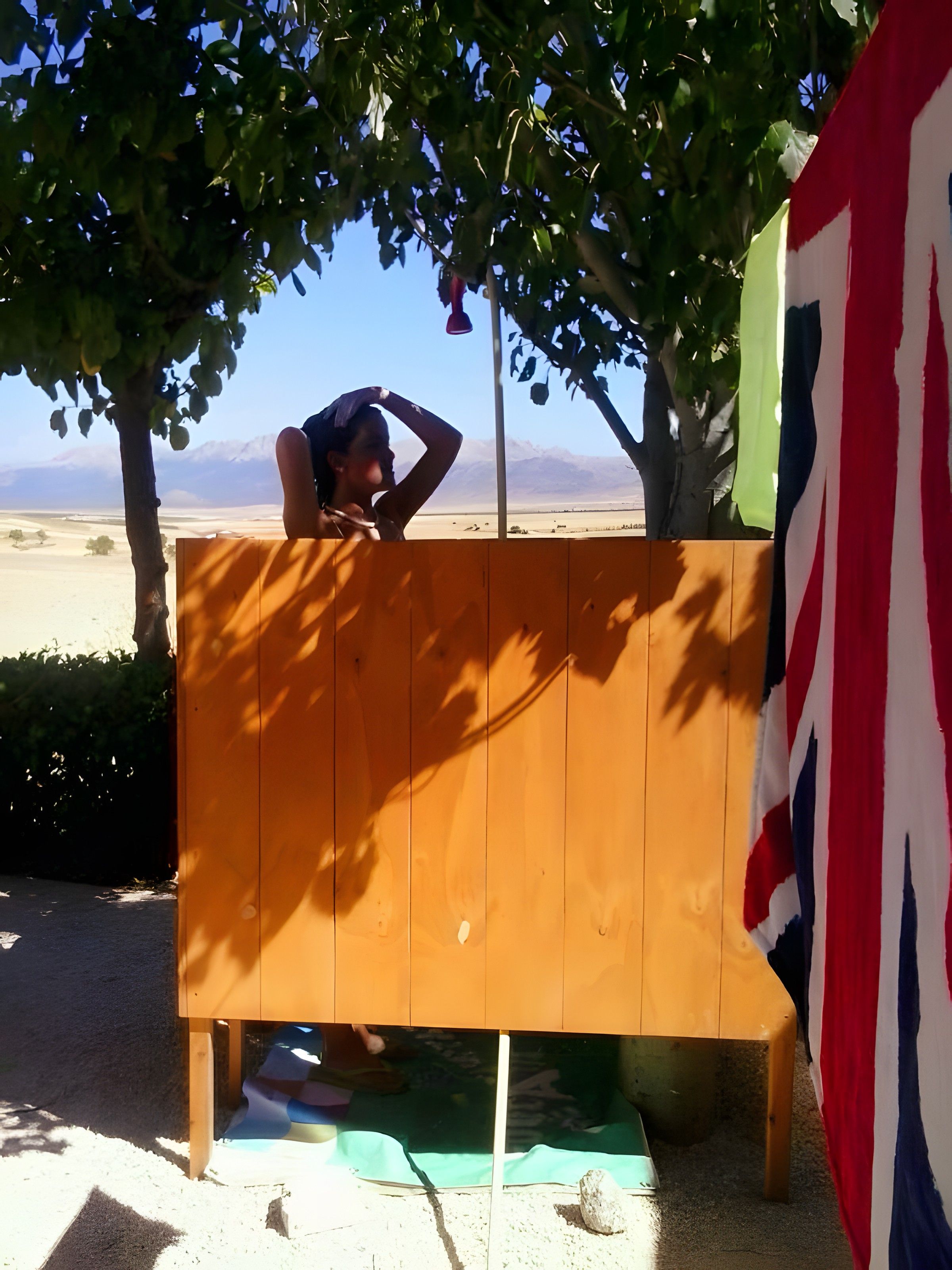 Una estructura de madera con una persona debajo, una bandera y vista a un paisaje desértico.