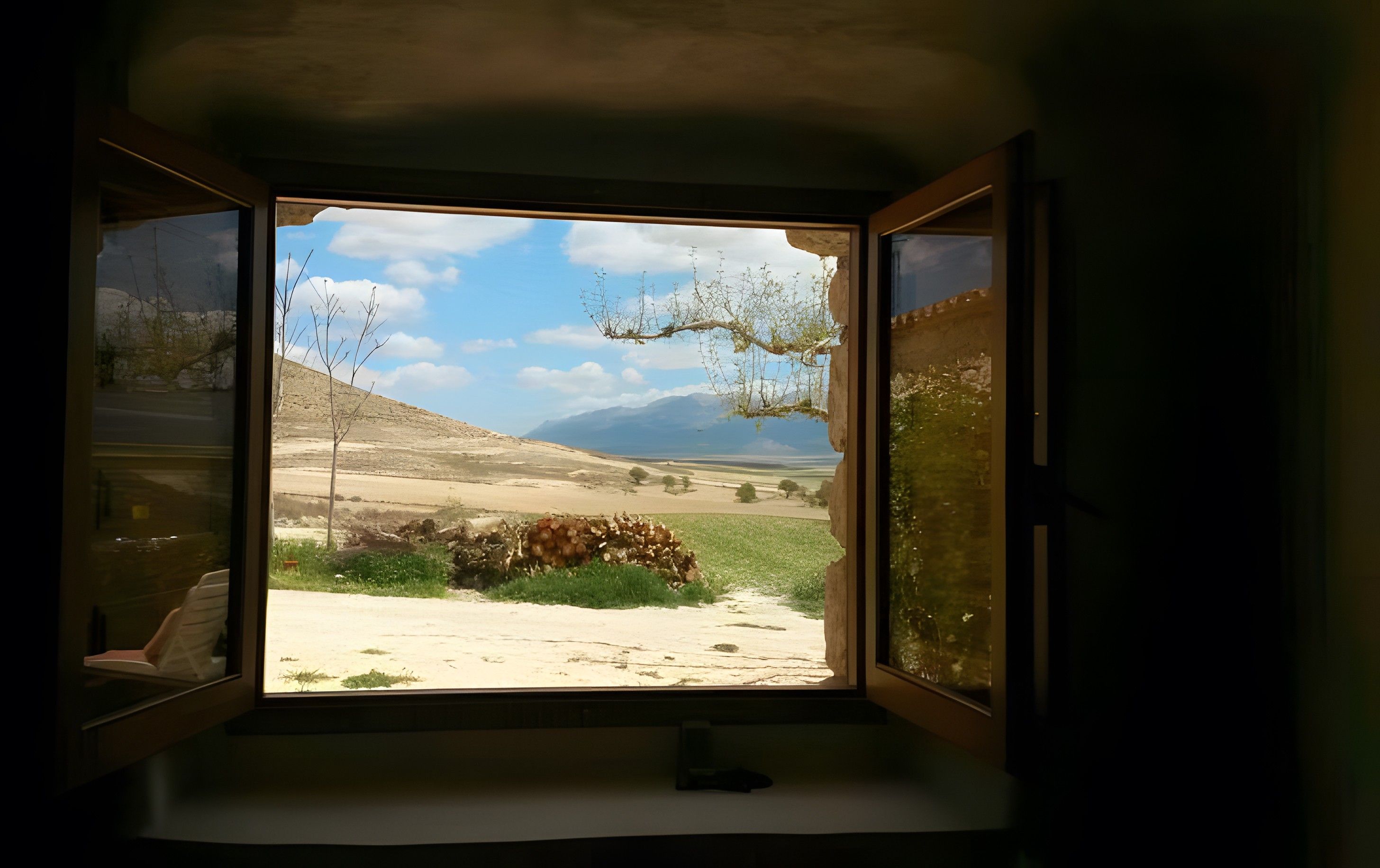 Una ventana con vista a un paisaje, que incluye una colina y un cielo despejado.