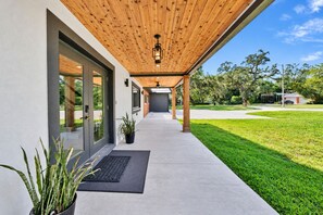 A covered outdoor walkway leading to a modern building with large glass doors and a wooden ceiling. - Casa Lumina | 6 Bedroom Luxury Estate | Pool, Spa & Outdoor Kitchen (Temple Terrace)