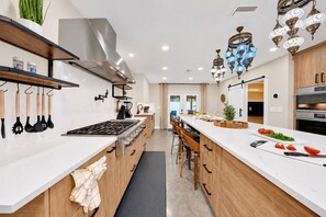 A modern kitchen with a central island, wooden cabinets, and a stainless steel range hood. - Casa Lumina | 6 Bedroom Luxury Estate | Pool, Spa & Outdoor Kitchen (Temple Terrace)