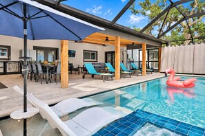 A pool area with lounge chairs, a flamingo float, and a covered patio with tables and chairs. - Casa Lumina | 6 Bedroom Luxury Estate | Pool, Spa & Outdoor Kitchen (Temple Terrace)