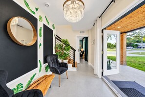 A modern interior with a blackboard wall, a round mirror, a black upholstered chair, a wooden bench, and a staircase leading to another room. - Casa Lumina | 6 Bedroom Luxury Estate | Pool, Spa & Outdoor Kitchen (Temple Terrace)