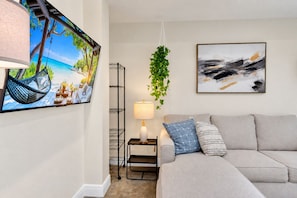 A living room with a sofa, a hanging plant, a lamp, and a painting on the wall. - Casa Lumina | 6 Bedroom Luxury Estate | Pool, Spa & Outdoor Kitchen (Temple Terrace)