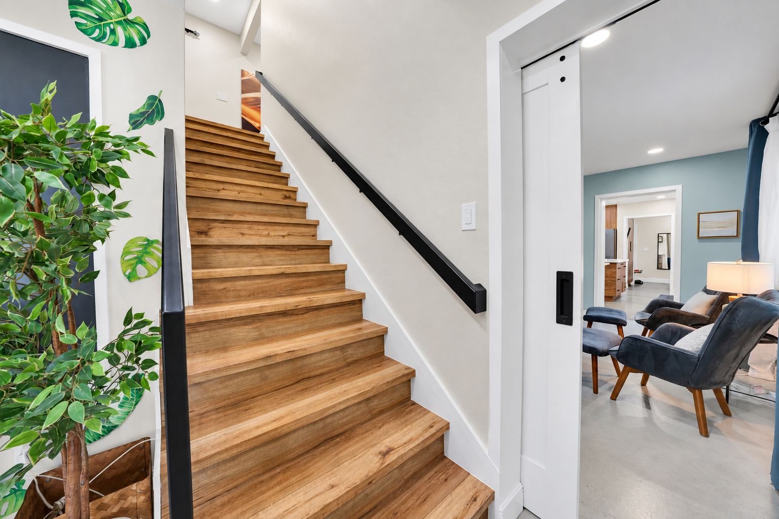 A wooden staircase with a black handrail leading to a room with a blue wall and a seating area with chairs.