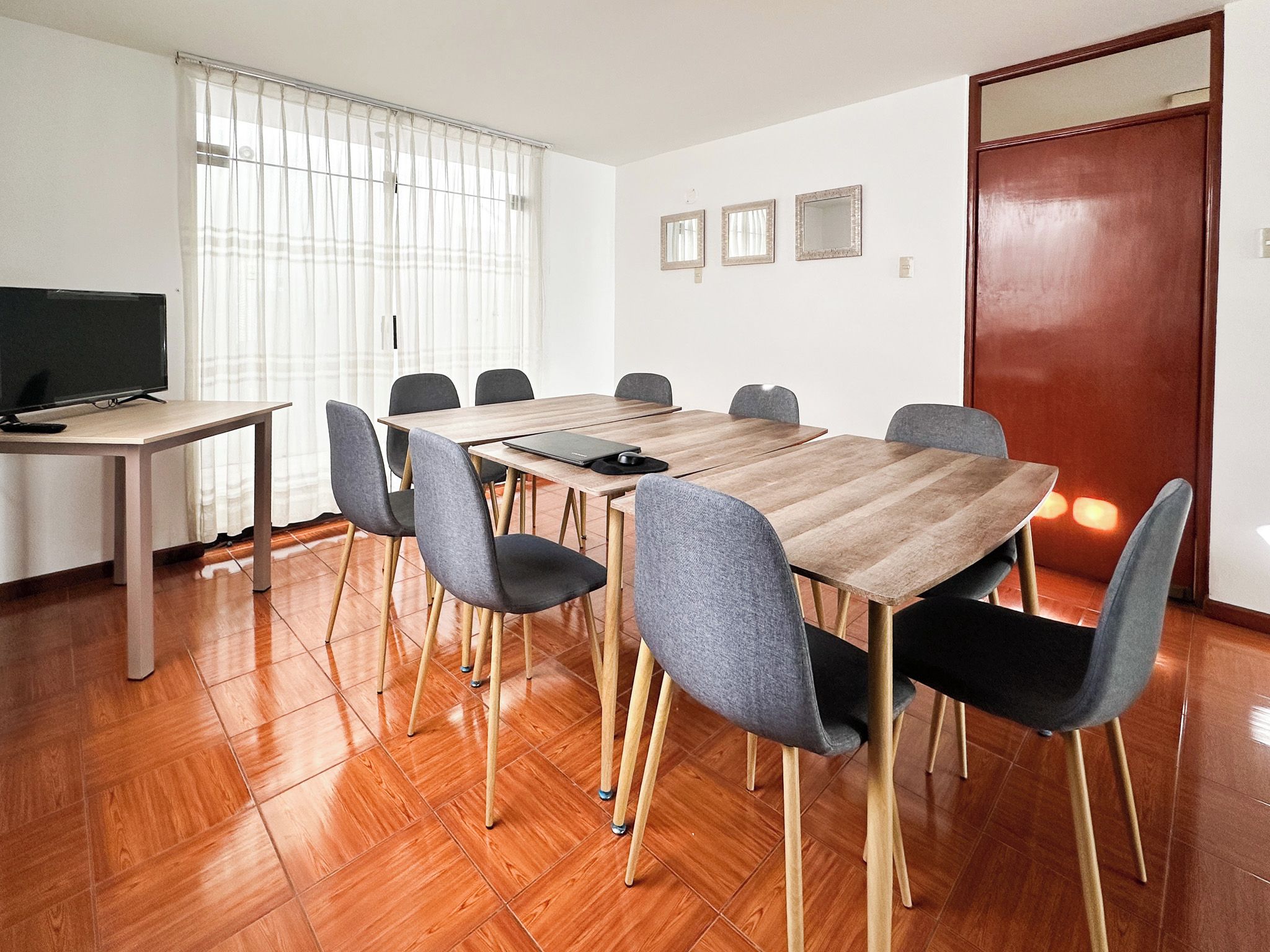 A conference room with a wooden table, grey chairs, a television, and a door.
