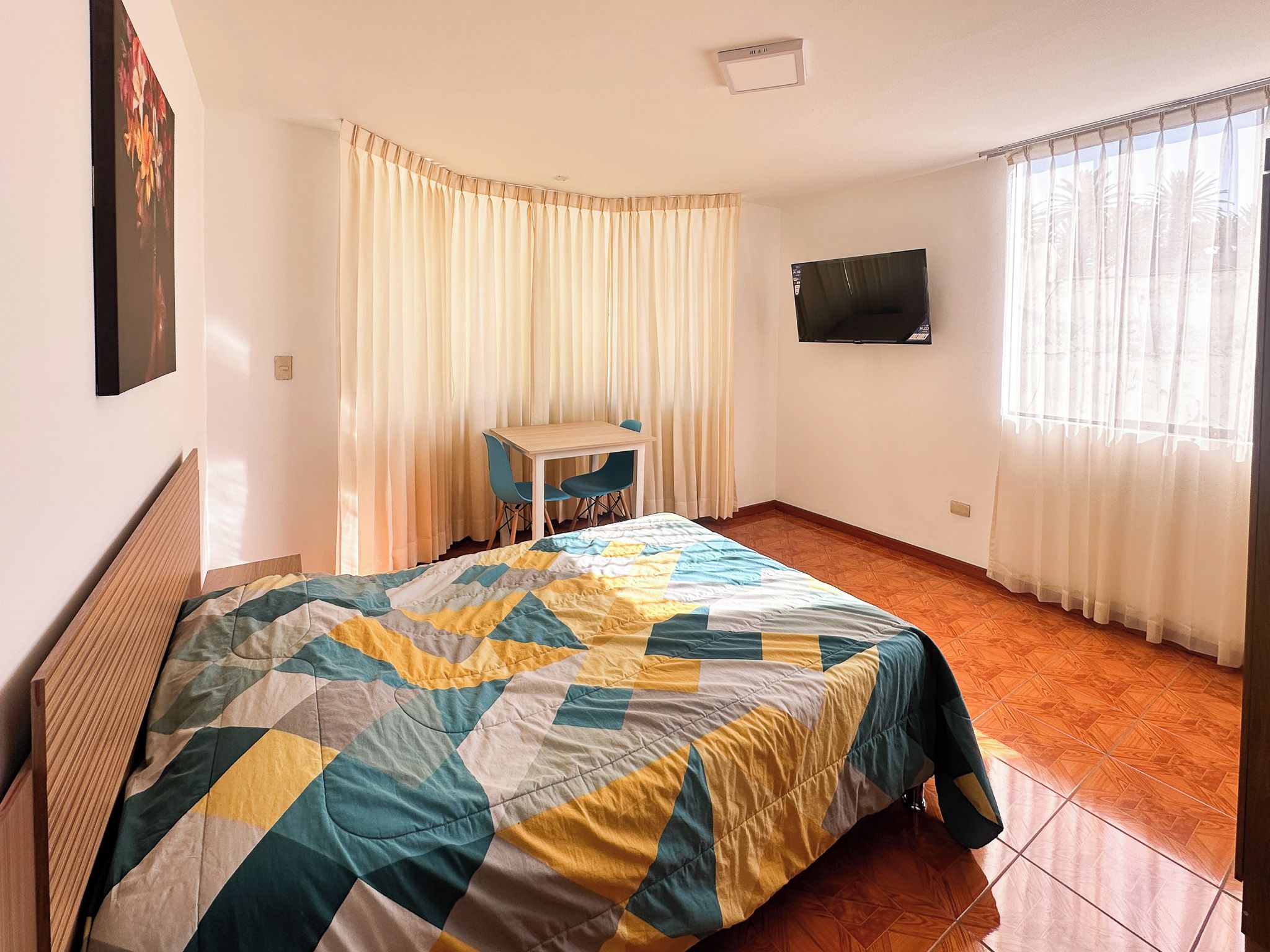 A room with a bed, a desk, a chair, a TV, and a window with curtains.