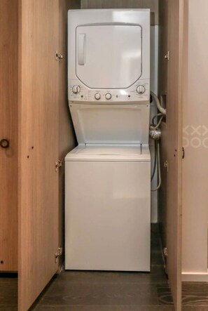 A compact, white washing machine in a narrow space with wooden doors and a tiled floor. - Stunning King Suite Brieckell (Miami)