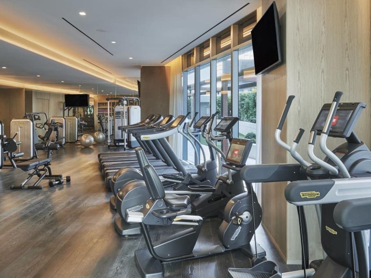 Une salle de sport équipée de plusieurs tapis de course, de machines de musculation et d’une grande fenêtre laissant entrer la lumière naturelle.
