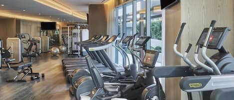 Un gimnasio con varias cintas de correr, máquinas de pesas y un amplio ventanal que proporciona luz natural.