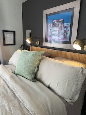 A bed with a headboard, two wall-mounted lamps, and a framed artwork above the bed.