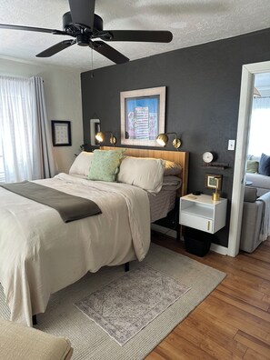 Une chambre à coucher avec un lit, des tables de chevet, un ventilateur de plafond, un tapis et un tableau encadré au mur.