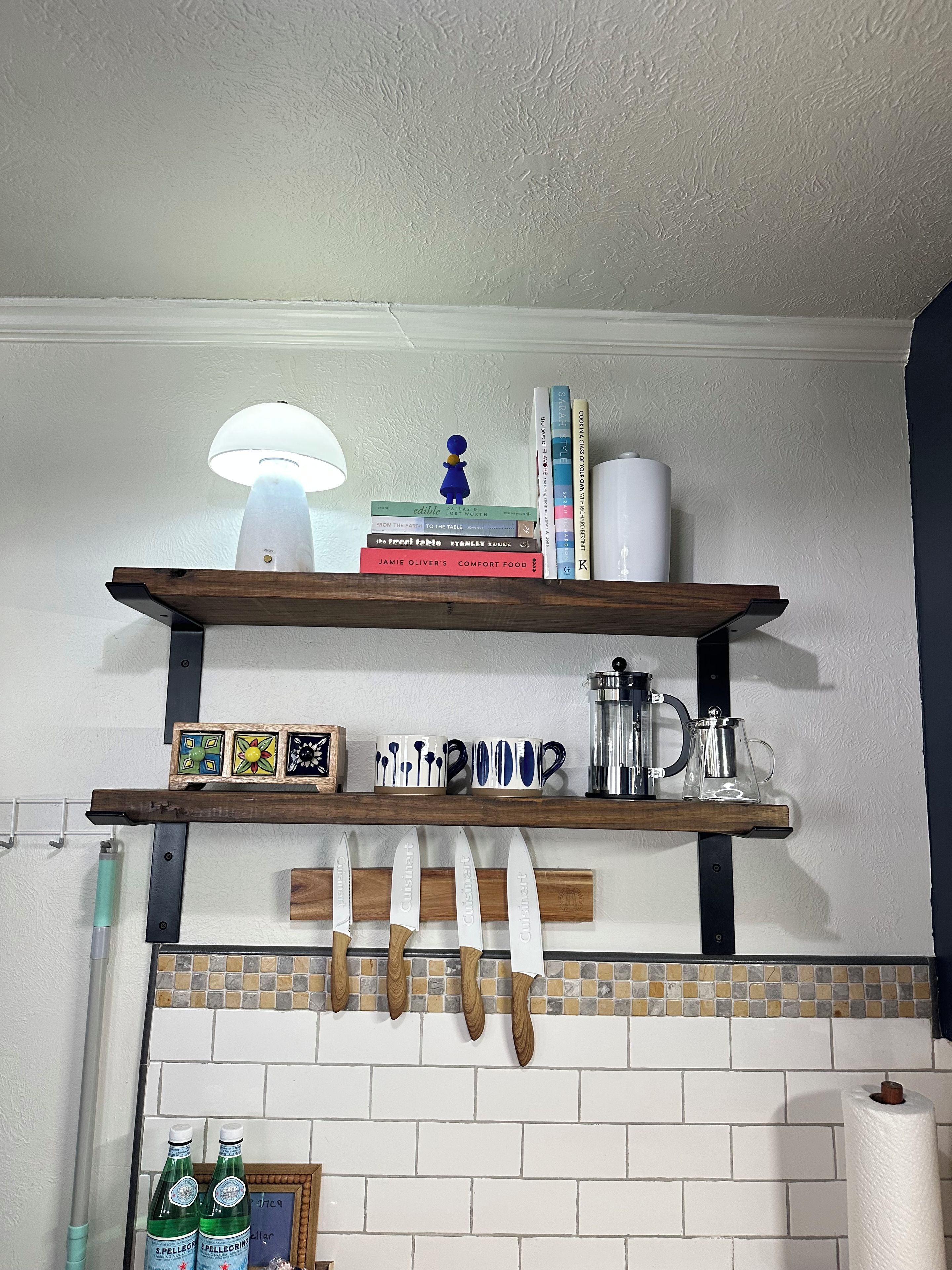 Une cuisine avec un mur en briques blanches, des étagères en bois, un porte-couteaux suspendu et un plafond blanc.