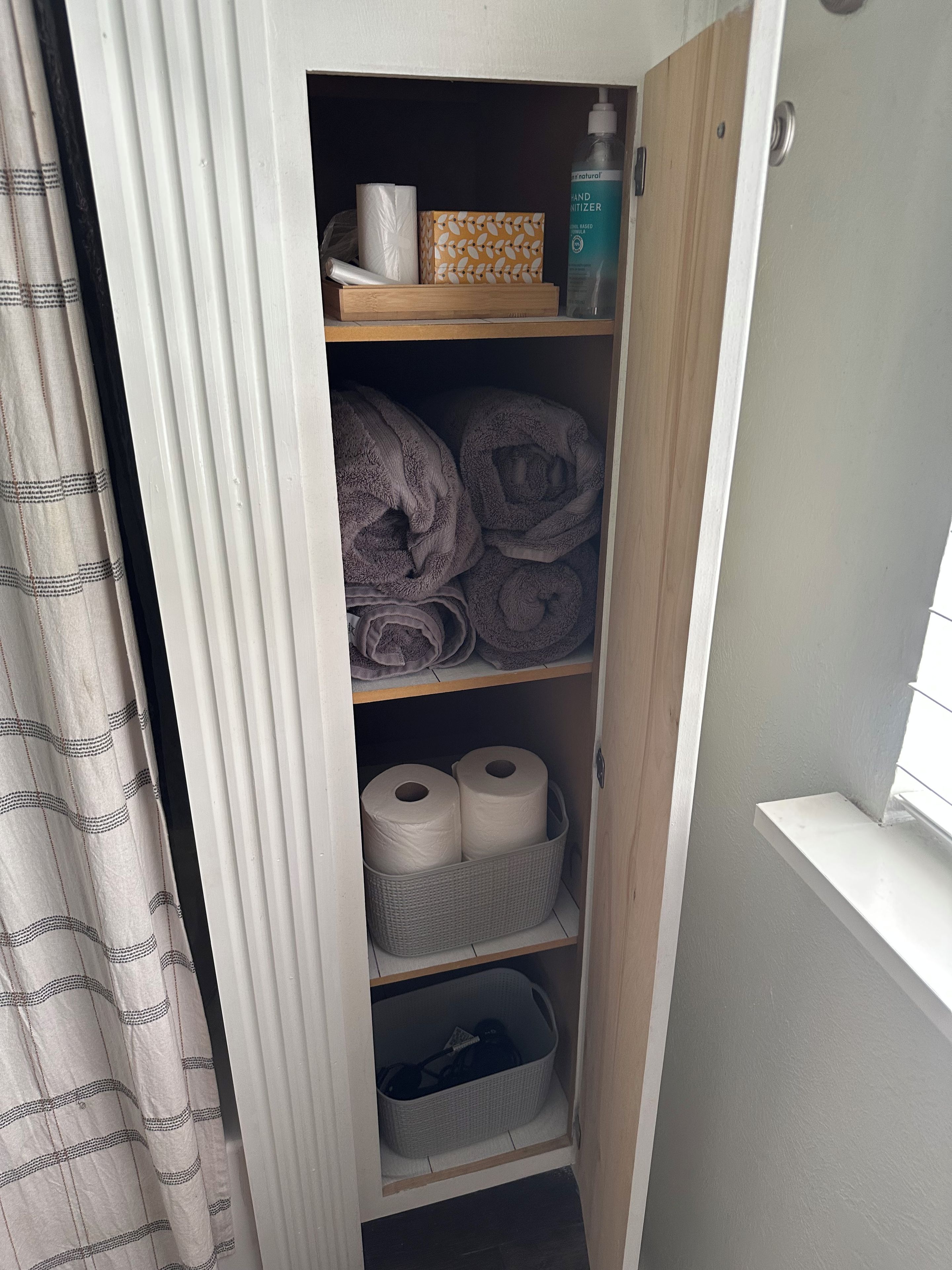 A storage closet with shelves holding towels, a box, and a bottle.