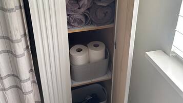 A storage closet with shelves holding towels, a box, and a bottle.