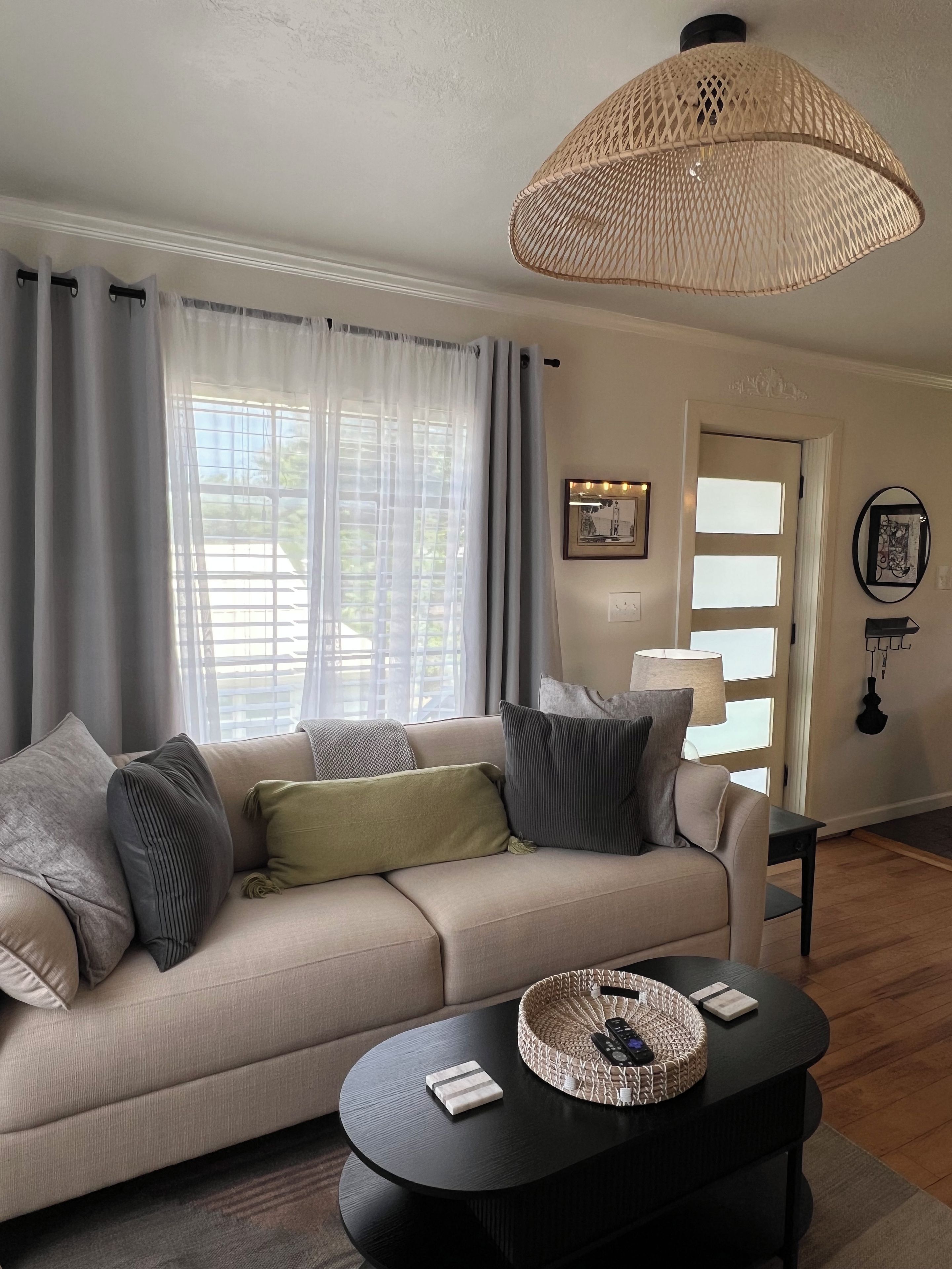 A living room with a sofa, a round coffee table, a woven lamp, and a door with a light switch.