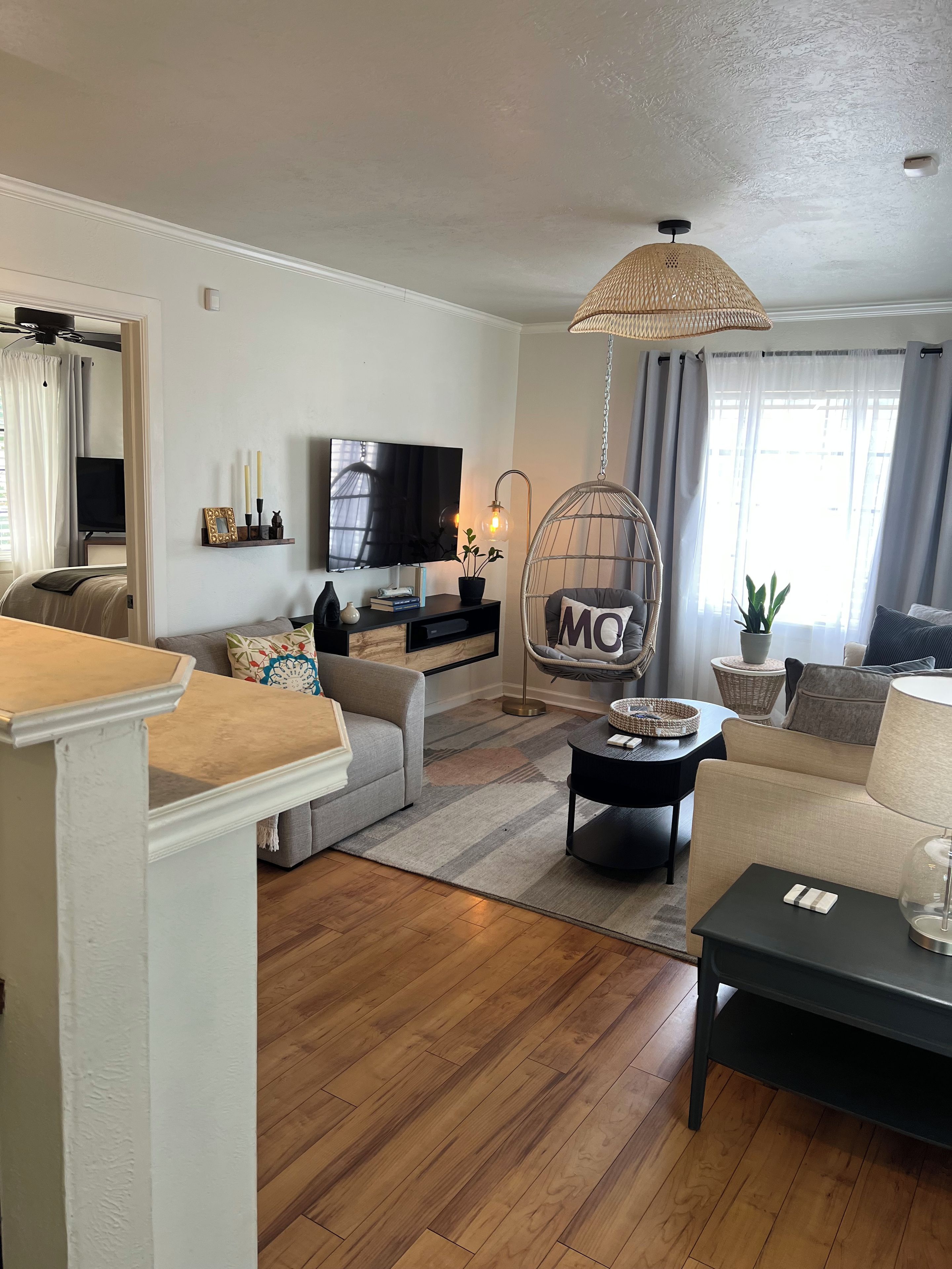 Een woonkamer met een bank, een salontafel, een televisie, een hangstoel en een groot raam met gordijnen.