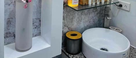 Une salle de bain avec un lavabo en marbre, un miroir rond et une étagère contenant des articles de toilette.