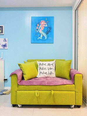 A room with a green sofa, a blue wall, and a framed artwork above the sofa. - 1BR Premium Suite w Patio (Paranaque)