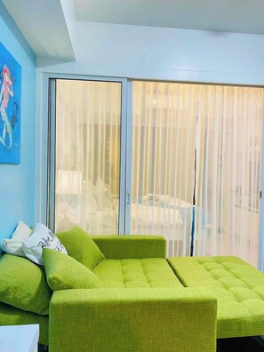 A room with a green sofa, a white pillow, and a blue wall. - 1BR Premium Suite w Patio (Paranaque)