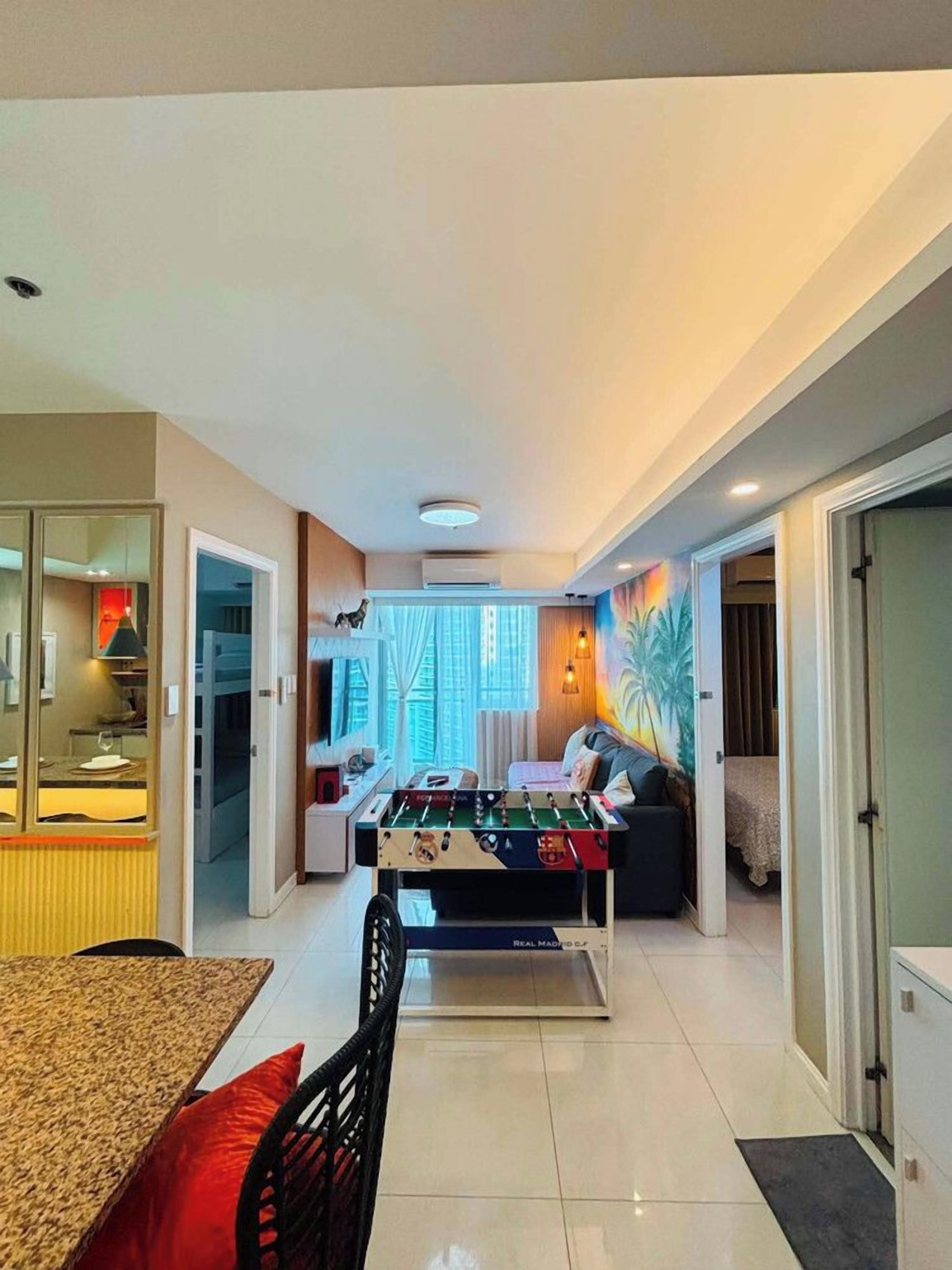 A modern living room with a foosball table, a dining area with a table and chairs, and a kitchen in the background.
