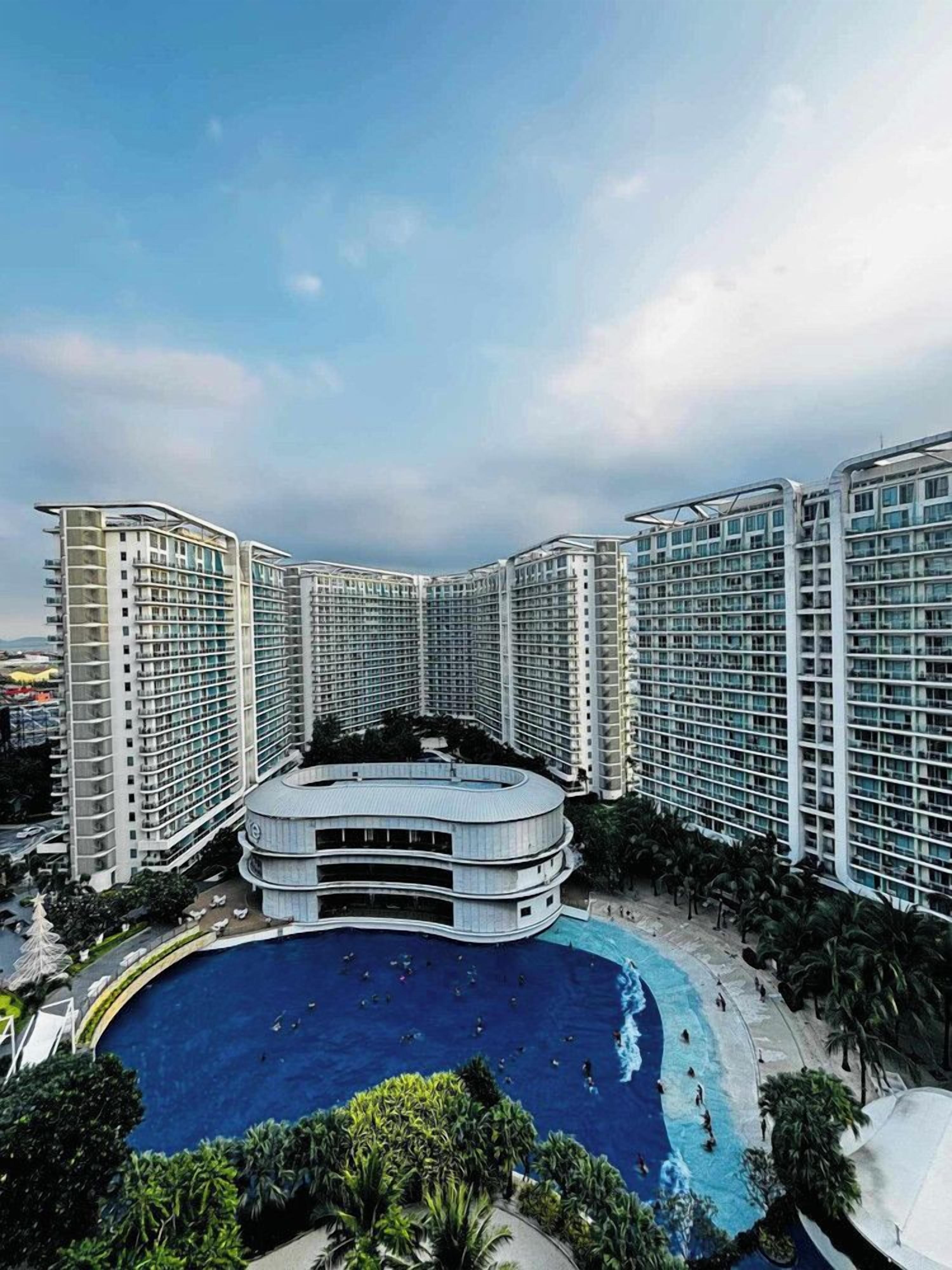 A high-rise hotel with multiple balconies, a central pool, and surrounding greenery.
