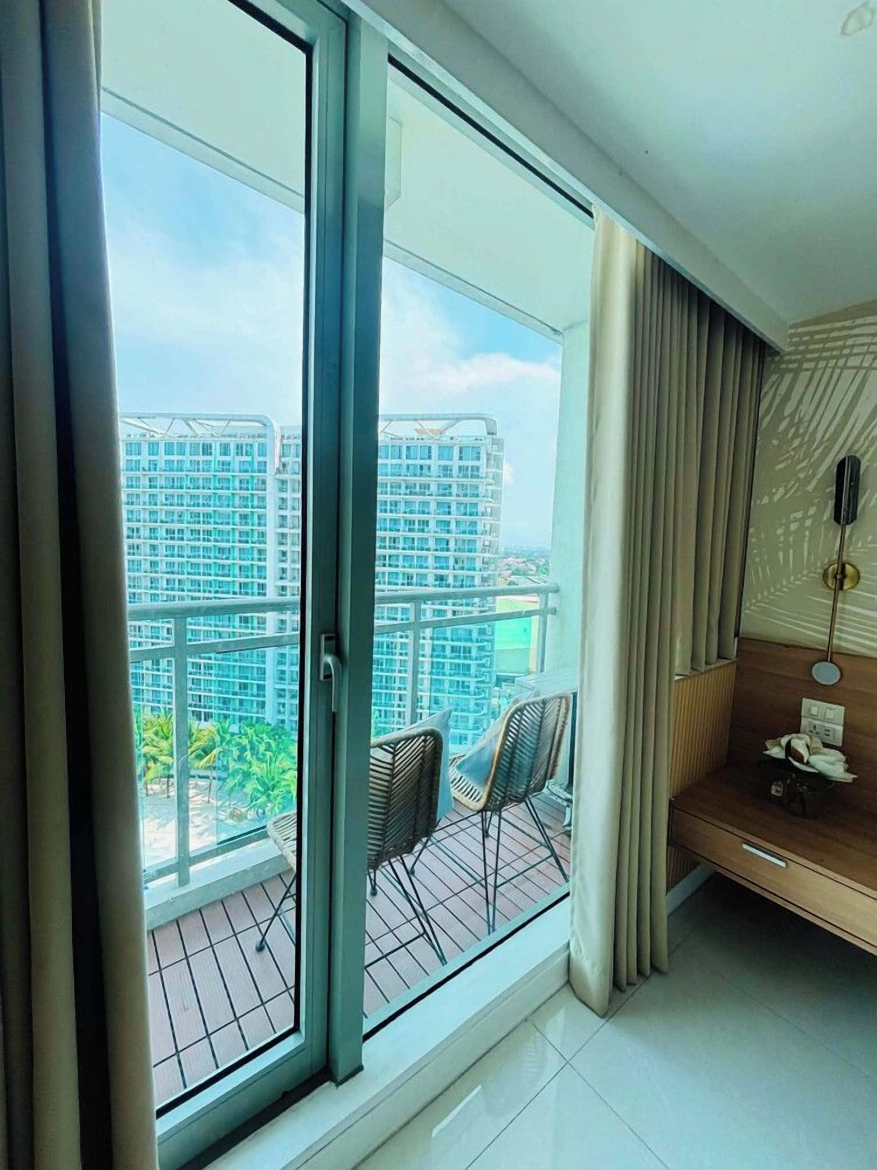 A modern room with a sliding glass door leading to a balcony, a small seating area with a chair, and a wooden cabinet.