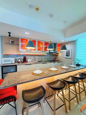 A modern kitchen with a central island, bar stools, pendant lighting, and a microwave. - 2BR Tropical Scandi Suite (Paranaque)