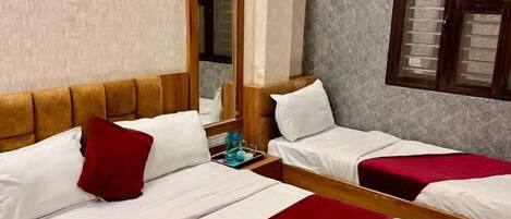 A hotel room with two beds, a wooden headboard, a mirror, and a window with blinds.