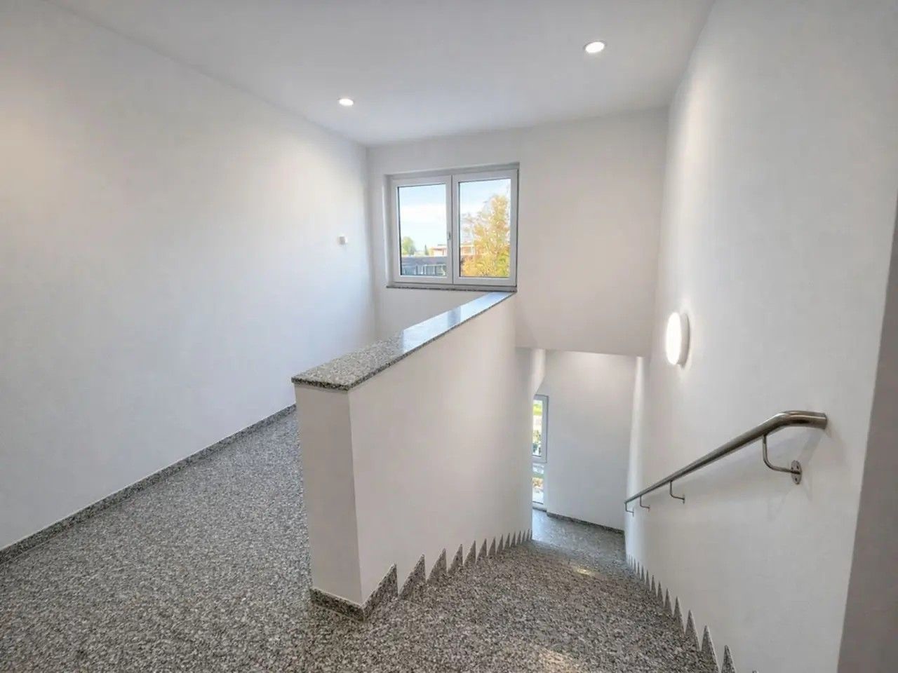 Eine Treppe mit Handlauf, einer kleinen Aussichtsplattform und einem Fenster für natürliches Licht.